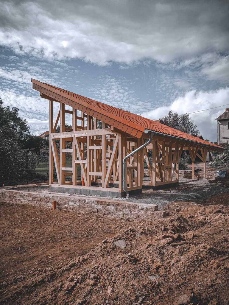 Außenansicht eines neuen Fachwerk-Gartenhauses in Heusweiler: Massive Holzkonstruktion mit rotem Pultdach und montierter Dachrinne.