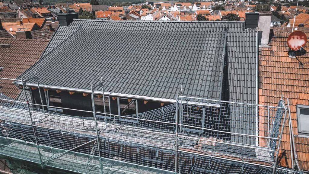 Detailansicht der neuen Dacheindeckung in Neunkirchen: Dunkle Dachziegel und eine großflächige, komplett modernisierte Dachgaube mit Schieferverkleidung.