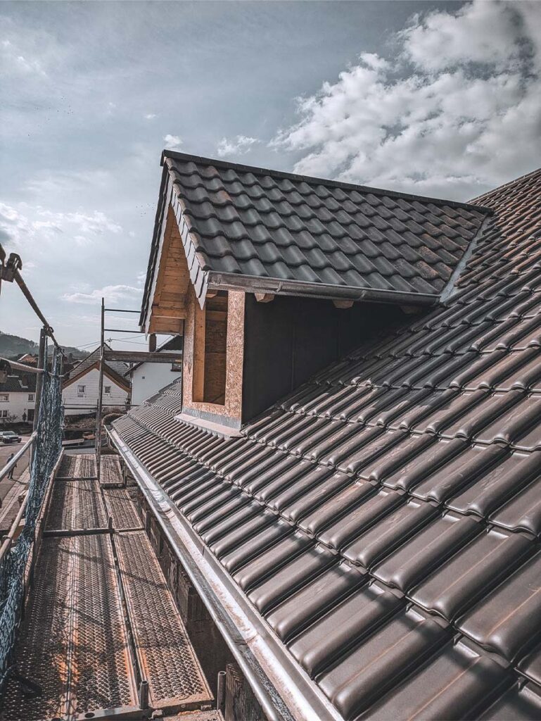 Fachgerecht neu eingedecktes Steildach mit dunklen Dachziegeln und einer Dachgaube neben einem Baugerüst