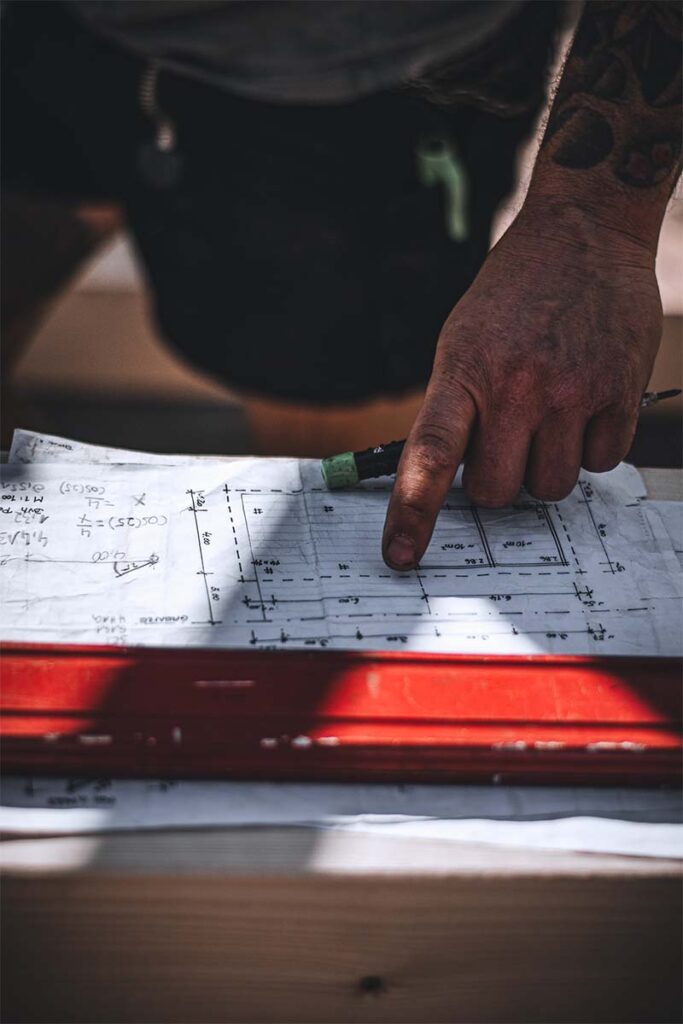 Nahaufnahme: Ein Dachdecker prüft auf der Baustelle Details und Maße auf einem handgezeichneten Bauplan